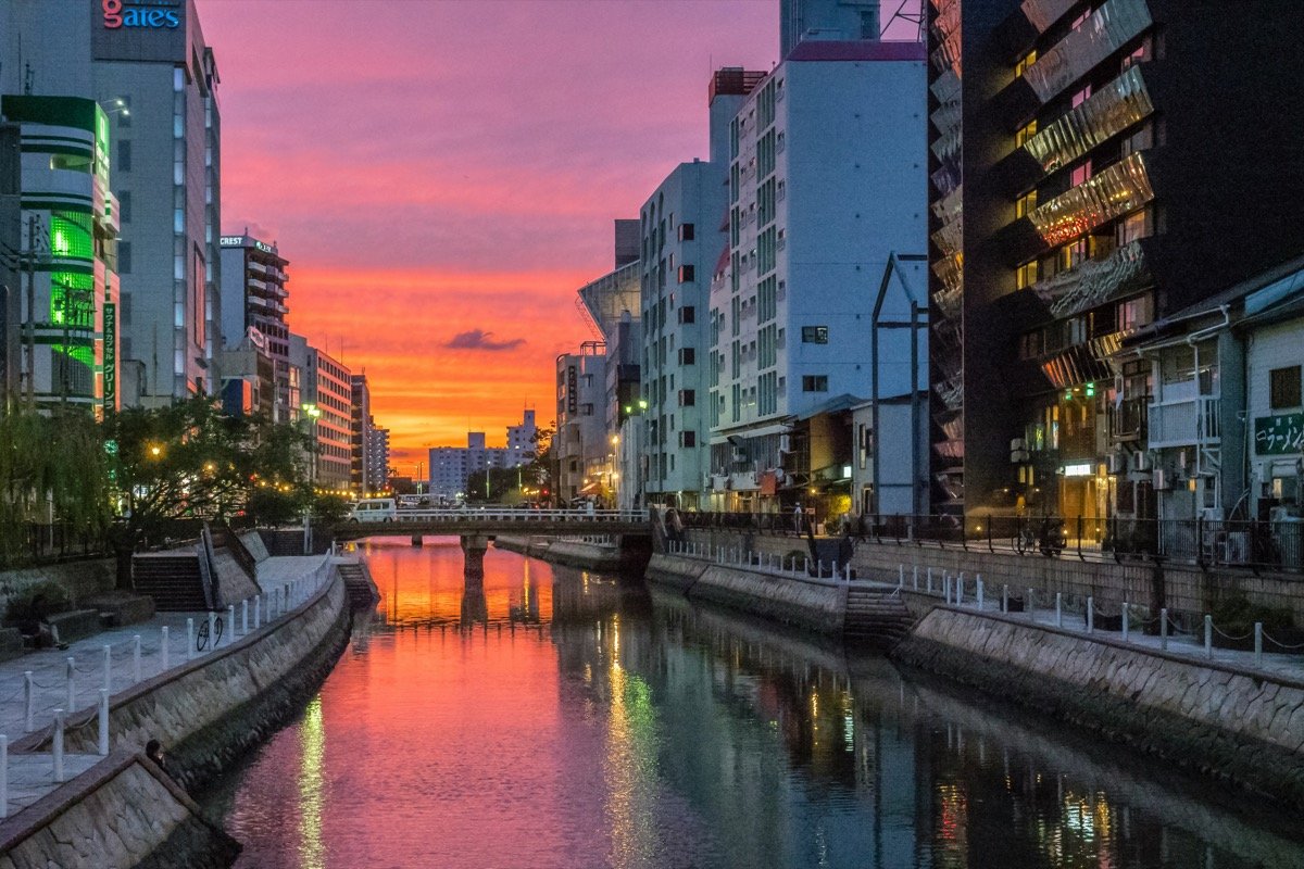 Fukuoka city canal at sunset with reflections of neon signs and buildings in the water