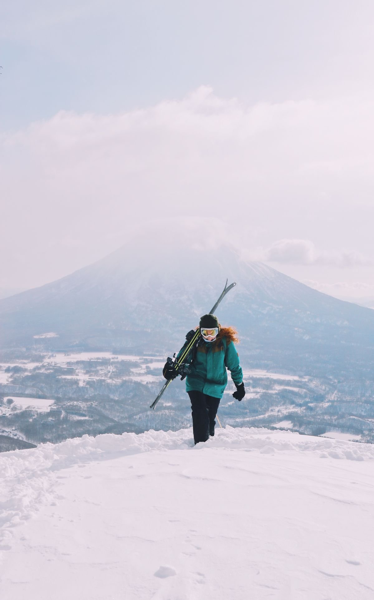 Skier carrying skis across open powder terrain with Mount Yotei in the background, Niseko, Hokkaido, Japan