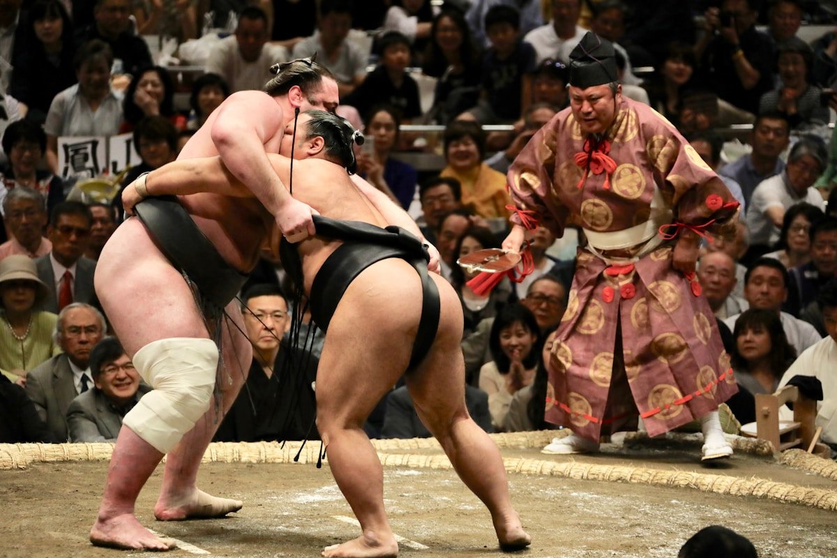 Two sumo wrestlers competing in a match with referee in ceremonial dress, Tokyo Japan