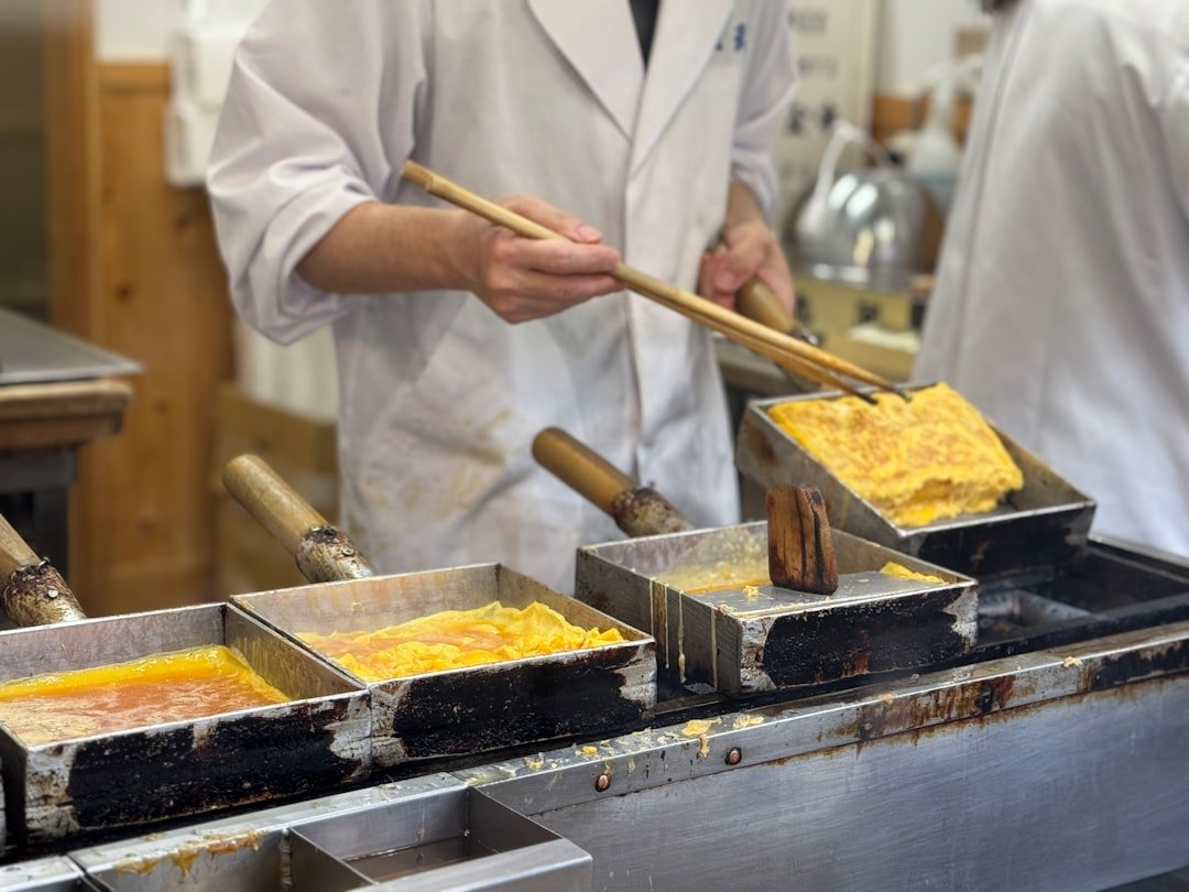 Chef in white coat using chopsticks to fold tamagoyaki in a rectangular Japanese omelette pan, Tokyo cooking class