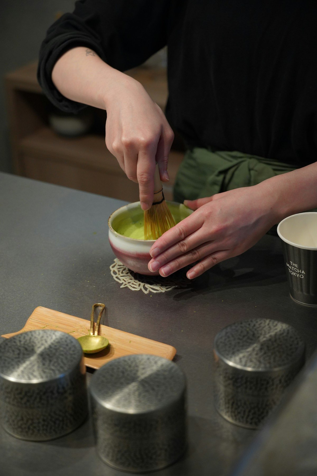 Hands whisking matcha tea with bamboo chasen in a ceramic chawan bowl — Tokyo tea ceremony experience, Japan