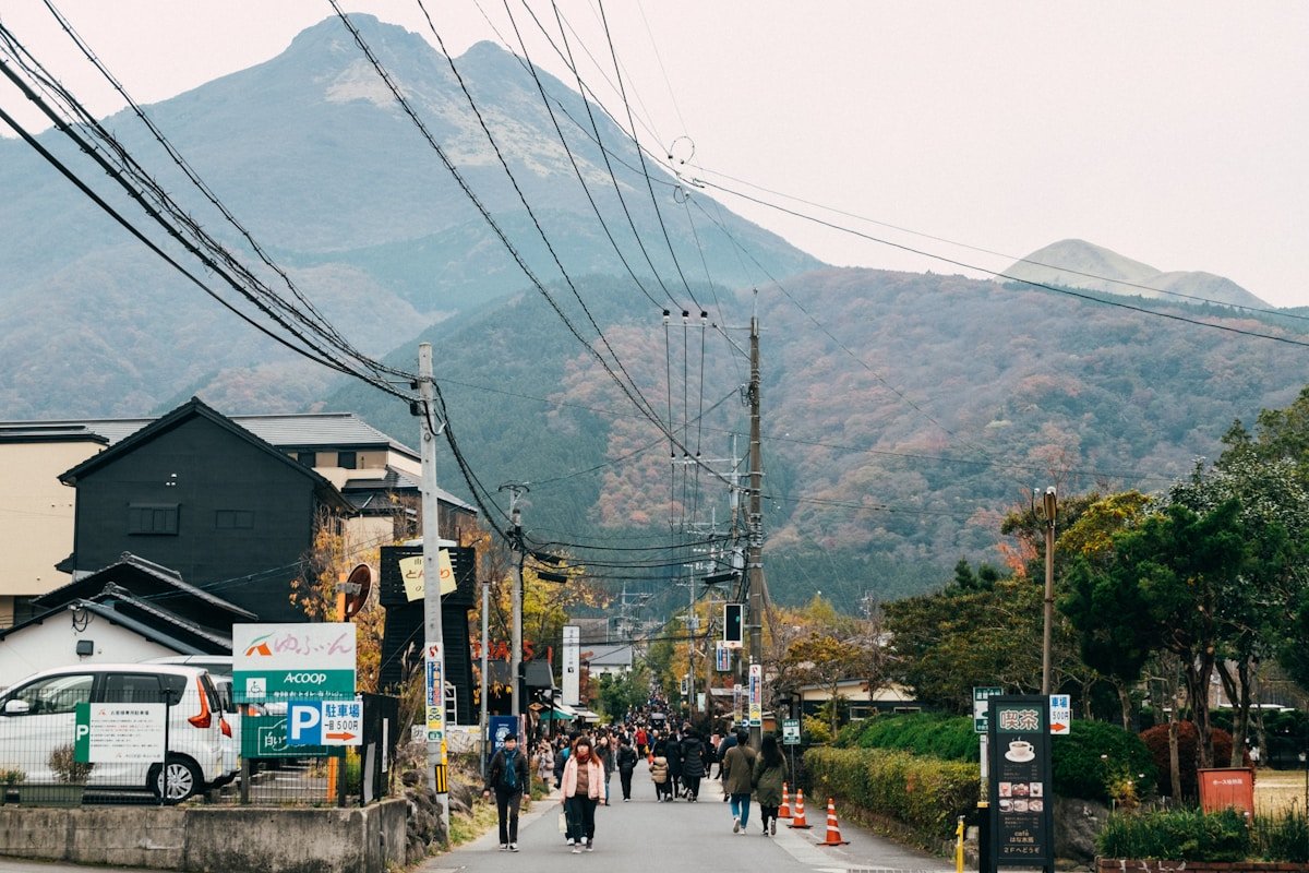 Visitors walking through Yufuin town with mountain backdrop, Oita, Japan