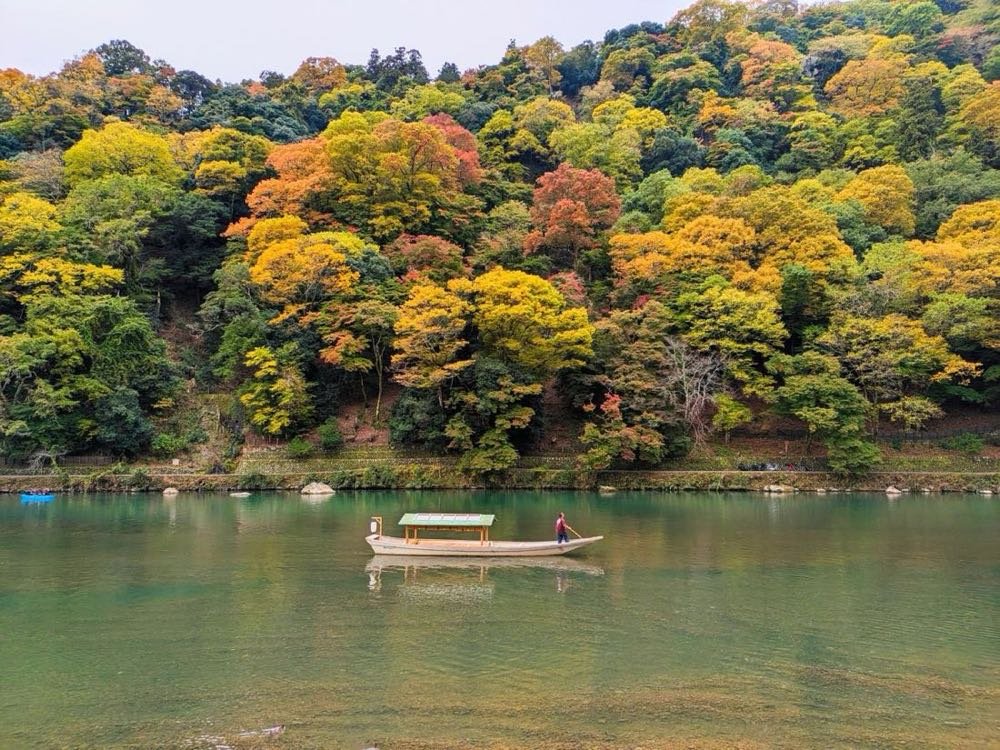 Autumn foliage on the hills above the Katsura River at Arashiyama with a boat