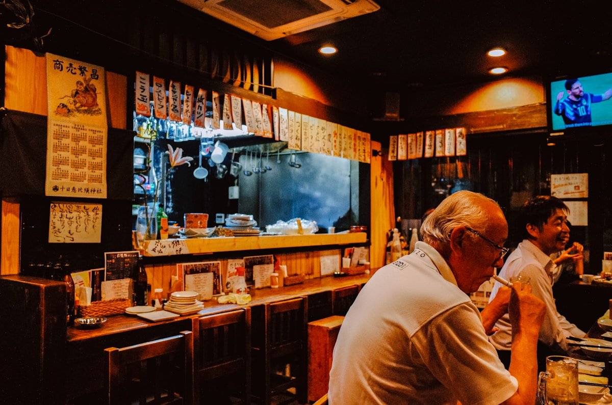 People sitting at a bar counter in a dimly lit Japanese restaurant