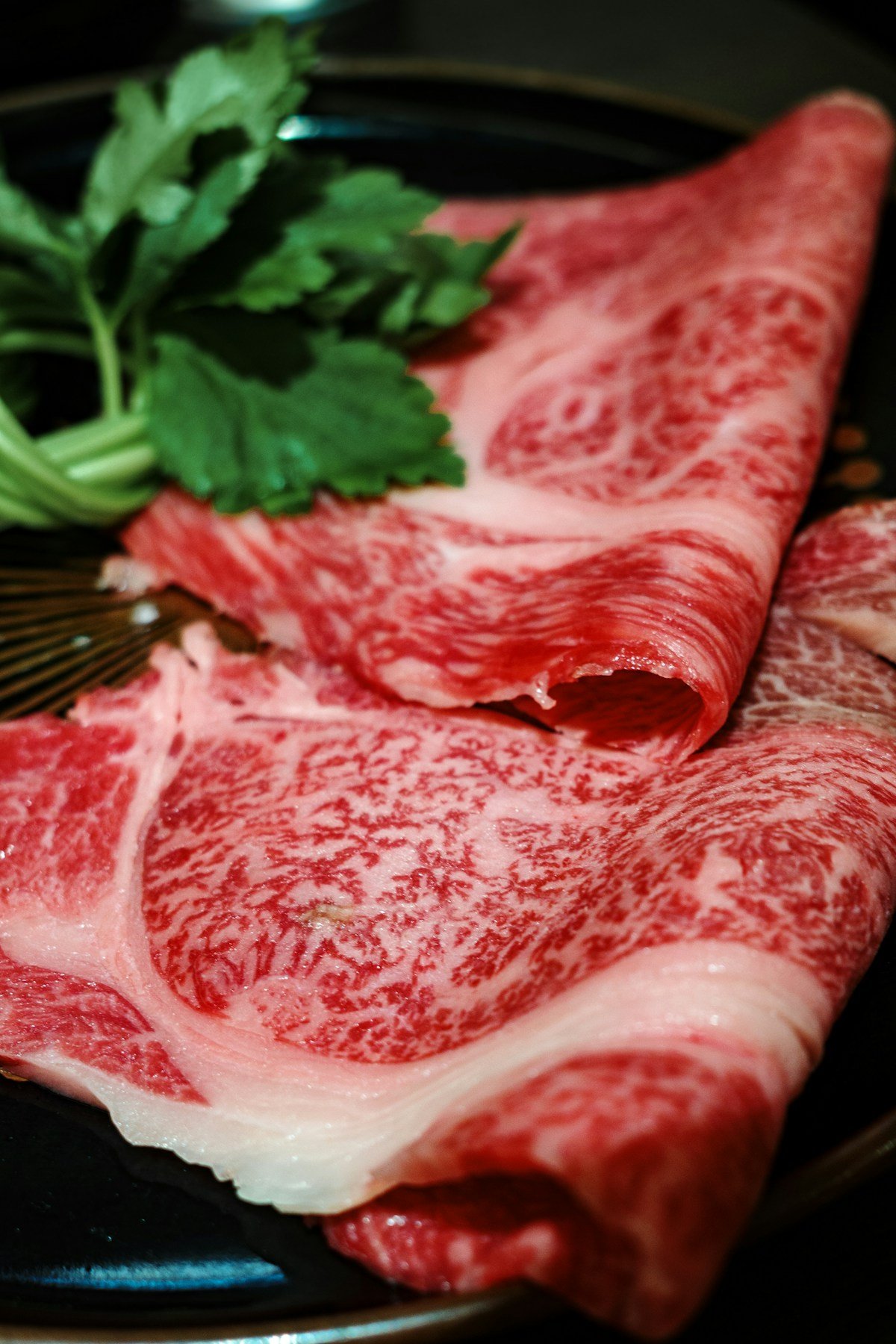 Thinly sliced marbled wagyu beef on a dark plate