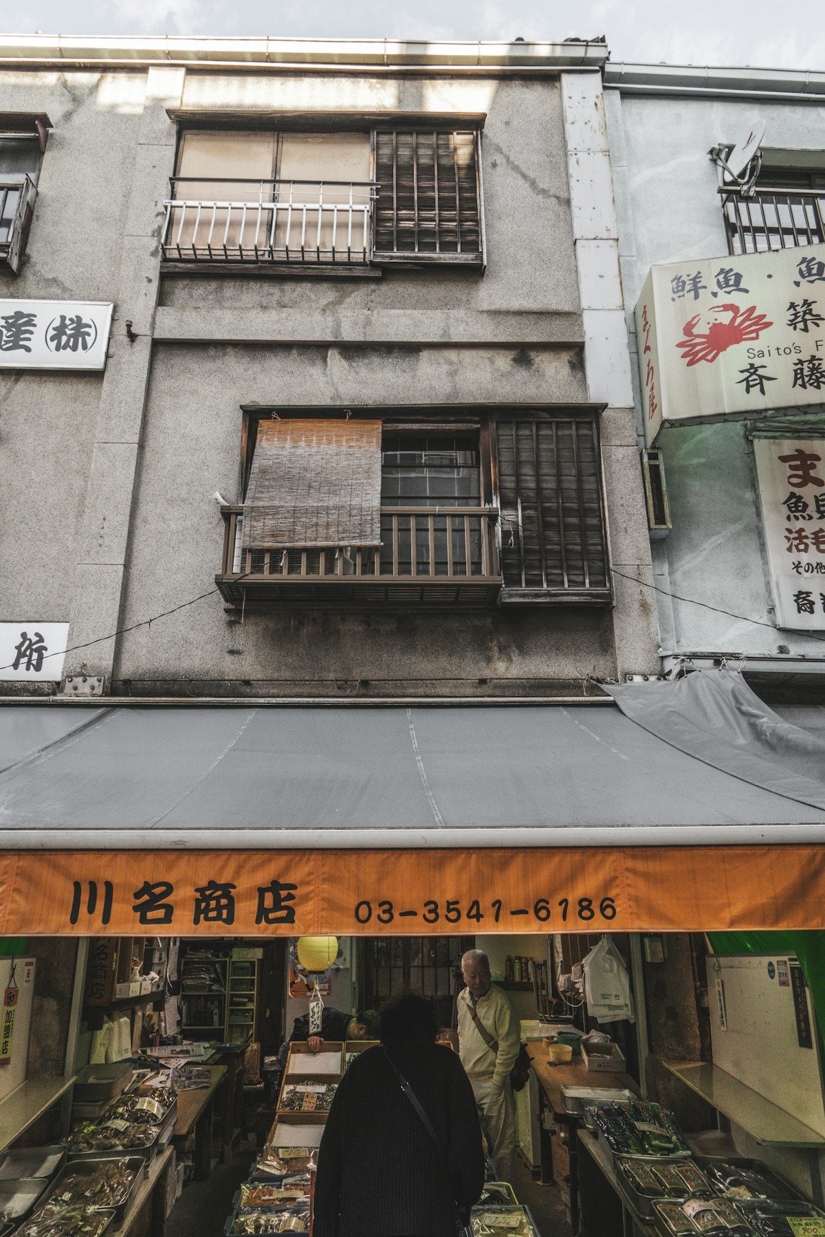 Shoppers at a traditional Japanese market stall with old buildings in a Tokyo shitamachi neighbourhood