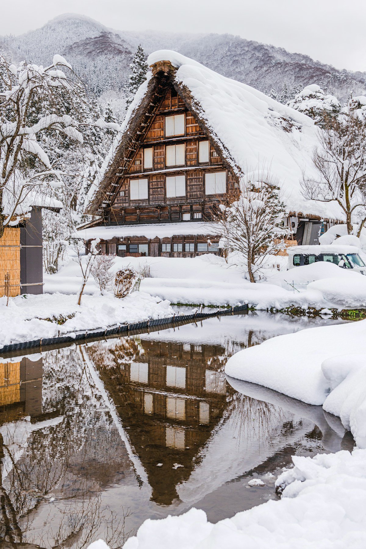 Snow-covered gassho-zukuri farmhouse reflected in a still pond at Shirakawa-go