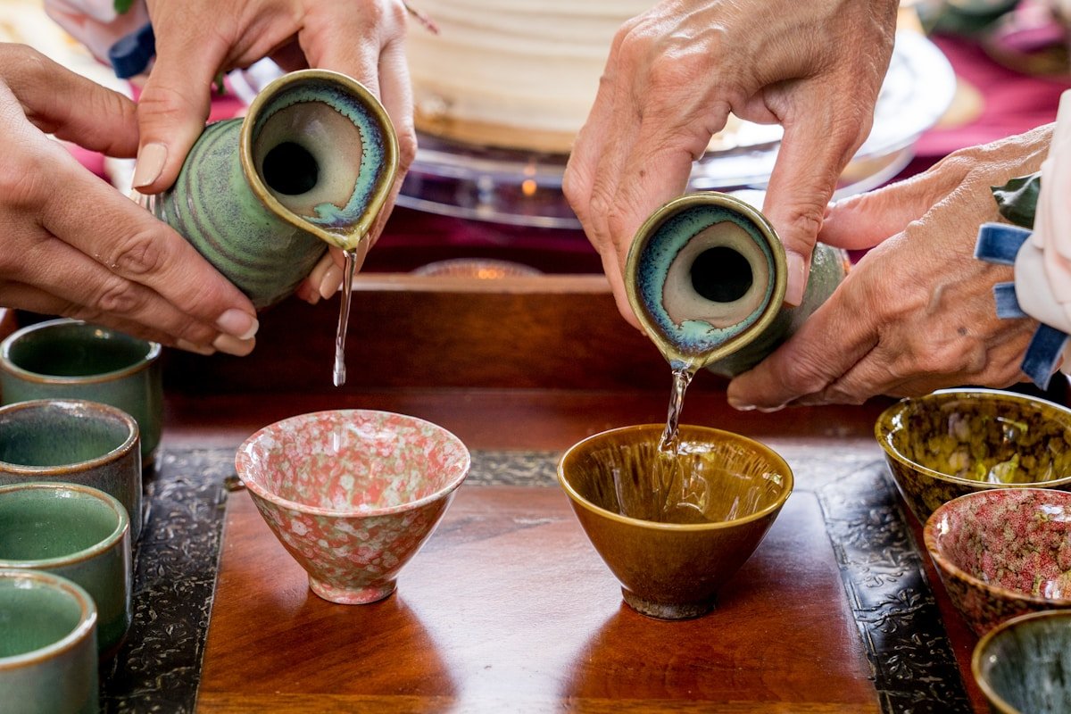 Sake being poured from ceramic tokkuri into small cups on a wooden tray