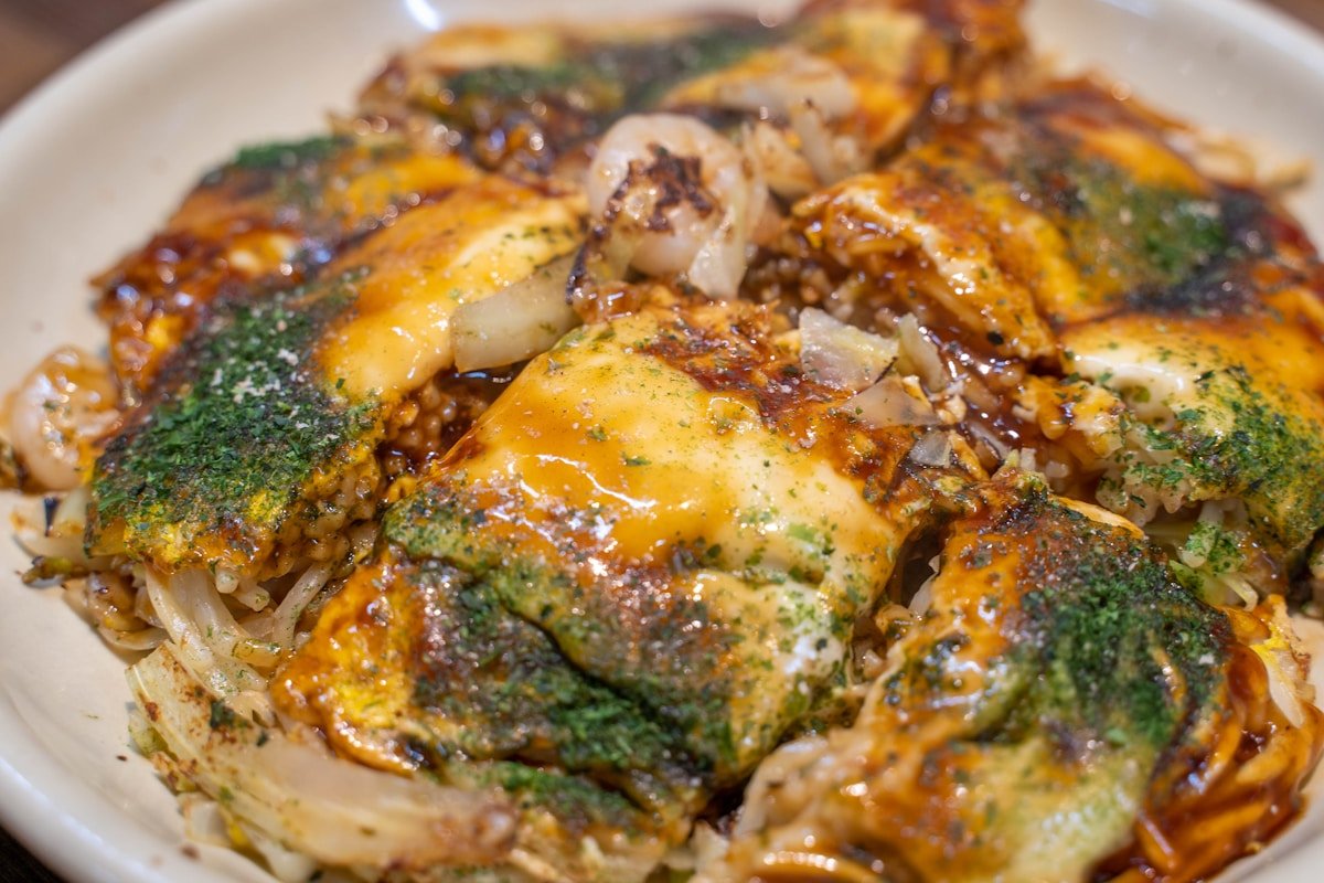 Hiroshima-style okonomiyaki being cooked on a teppan griddle with layered noodles