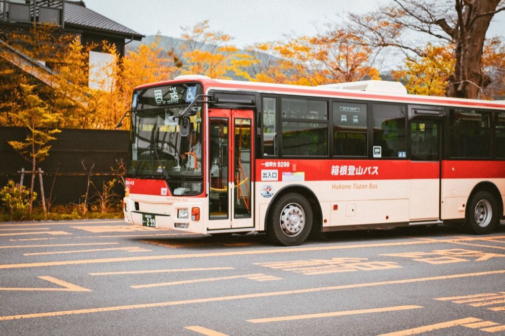 Red and white Hakone Tozan bus parked beside autumn trees