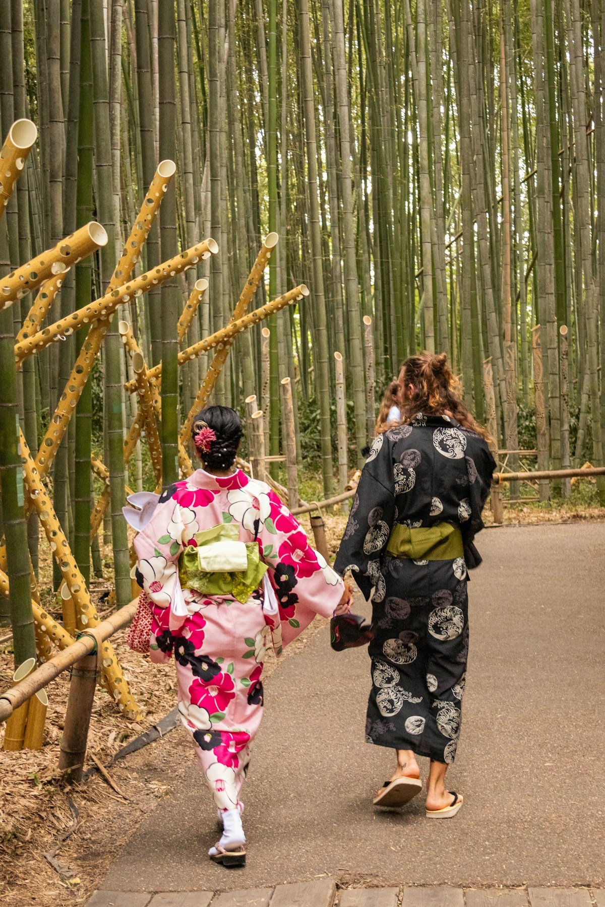 Couple in traditional kimonos walking hand in hand through Arashiyama bamboo forest, Kyoto, Japan