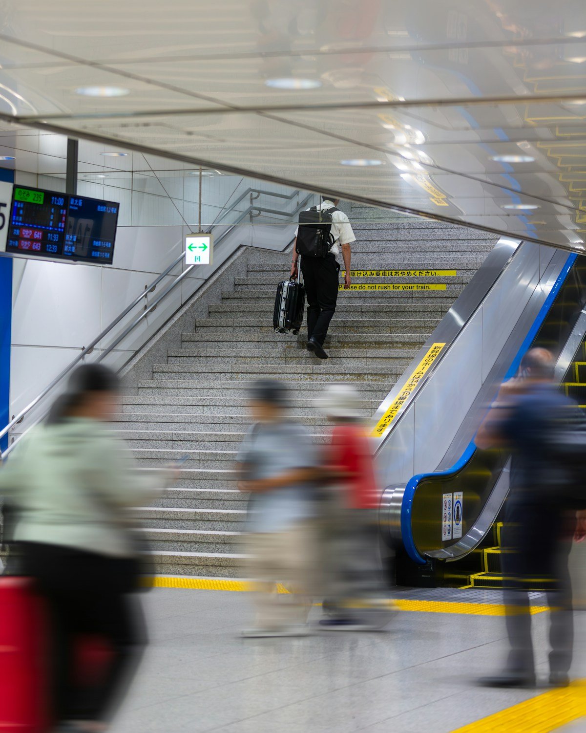 Traveller carrying suitcase up stairs at a busy Japanese train station